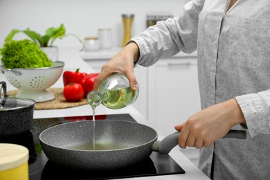 Woman pouring cooking oil from bottle into frying pan in kitchen, closeup