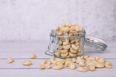 Photo of Glass jar with tasty cashew nuts on white wooden table. space for text