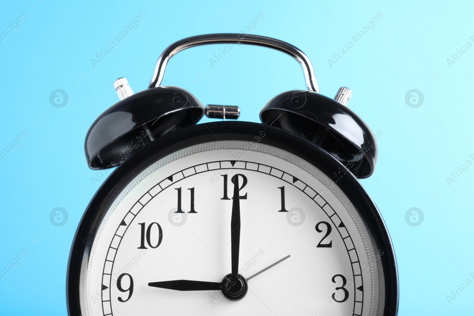 Photo of Black alarm clock on light blue background, closeup