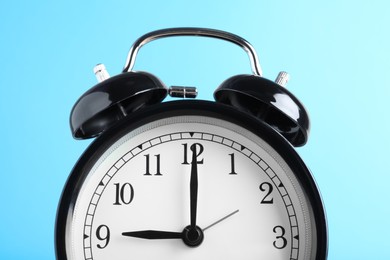 Black alarm clock on light blue background, closeup