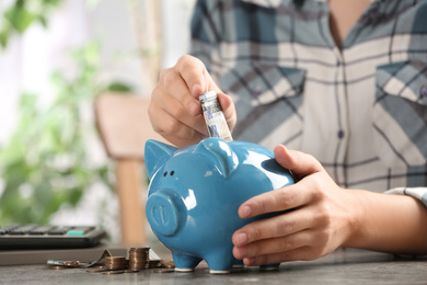 Photo of Woman putting money into piggy bank at table, closeup