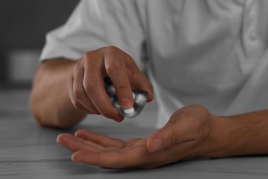 Man taking antidepressant pill out from blister at table, closeup