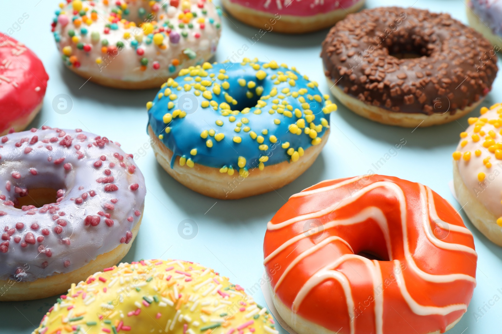 Photo of Delicious glazed donuts on light blue background, closeup