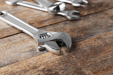 Photo of Adjustable wrench on wooden background, closeup with space for text. Plumber tools