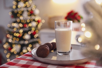 Photo of Glass of milk, chocolate cookies and blurred Christmas tree on background