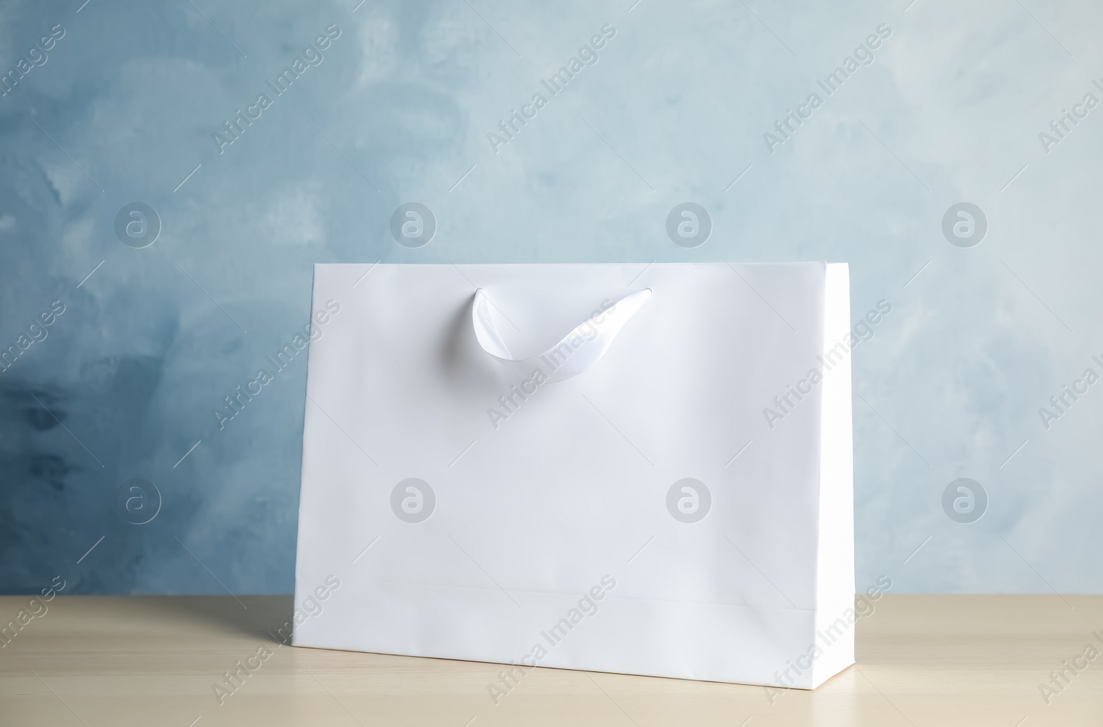 Photo of Paper shopping bag on table against color background. Mock up for design