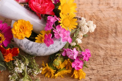 Photo of Marble mortar, pestle and different flowers on wooden table, closeup