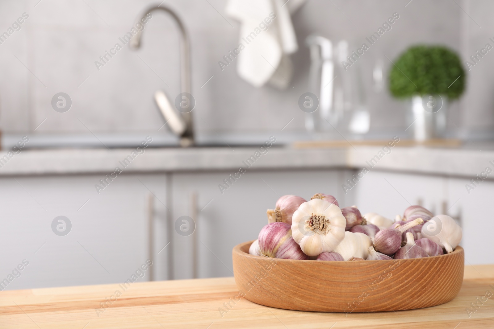 Photo of Bowl of fresh raw garlic on wooden table in kitchen, space for text