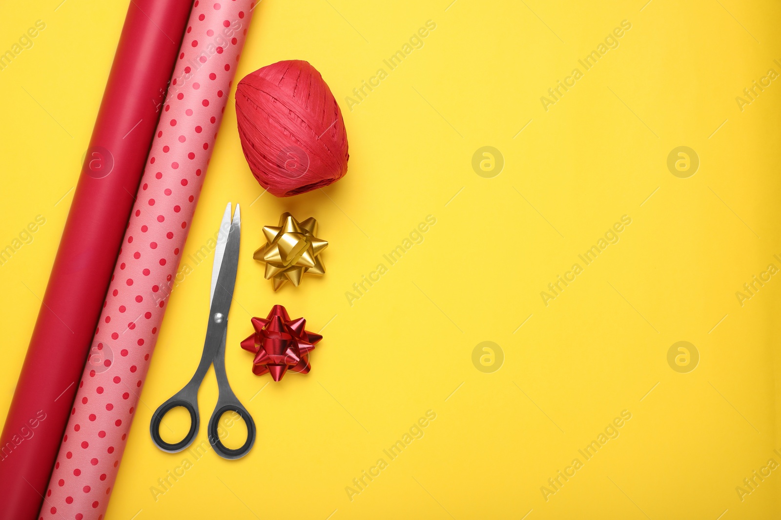 Photo of Rolls of colorful wrapping paper, bows and scissors on yellow background, flat lay. Space for text