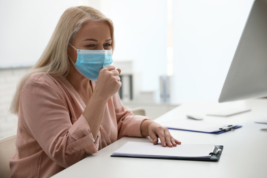 Photo of Mature woman wearing medical mask at workplace. Dangerous virus