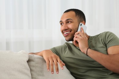 Photo of Smiling African American man talking on smartphone at home. Space for text