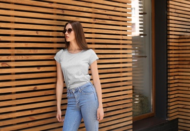 Photo of Young woman wearing gray t-shirt near wooden wall on street. Urban style