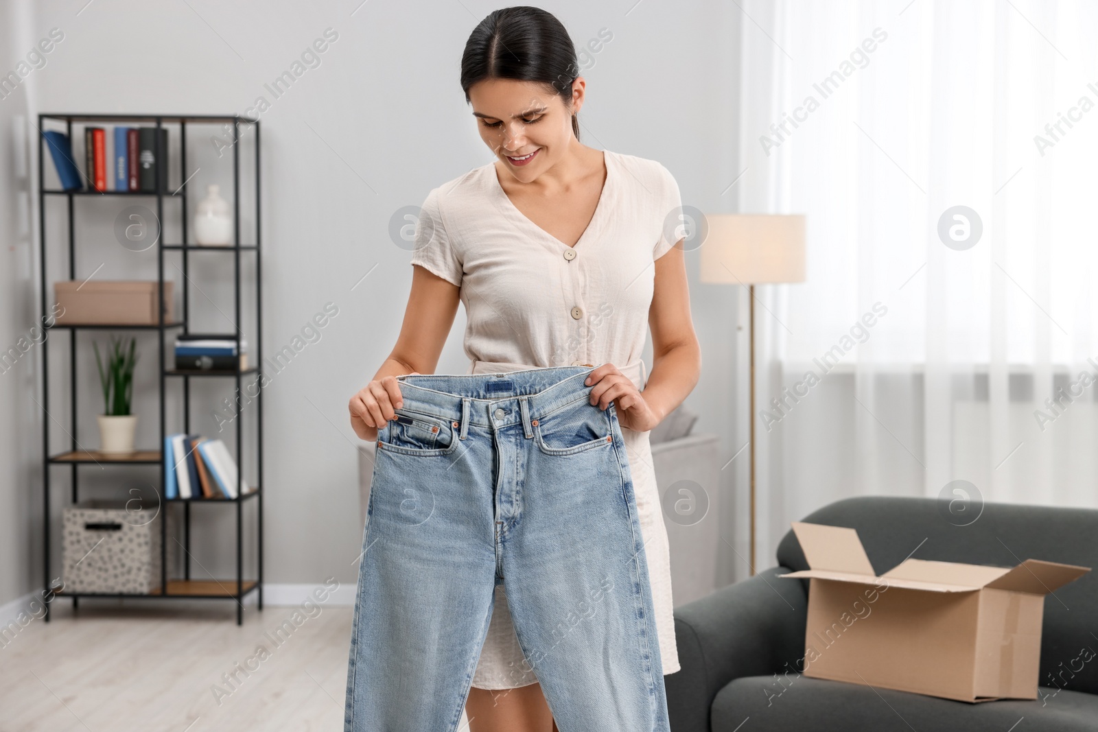 Photo of Young woman with just unpacked new jeans at home. Online shopping