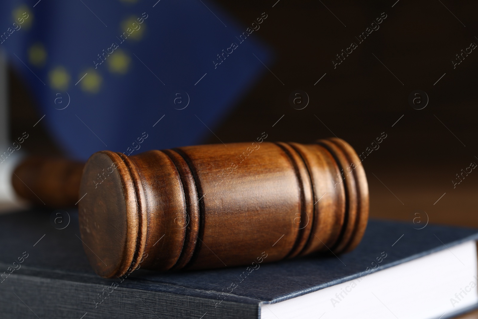 Photo of Wooden judge's gavel and book on table against European Union flag, closeup