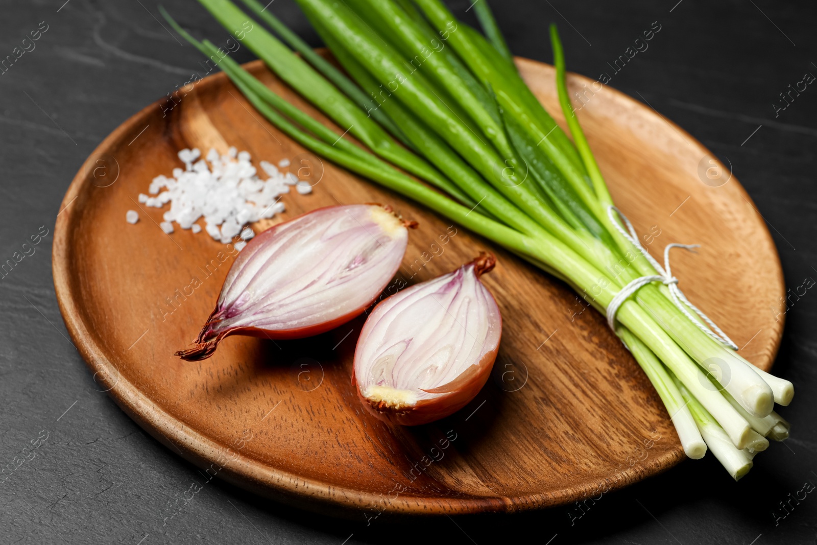 Photo of Bunch of fresh green onion and halved bulb on black table, closeup