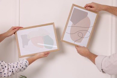 Man and woman hanging picture frames on white wall, closeup