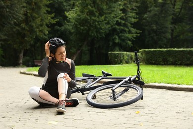 Young woman with injured knee near bicycle outdoors, space for text