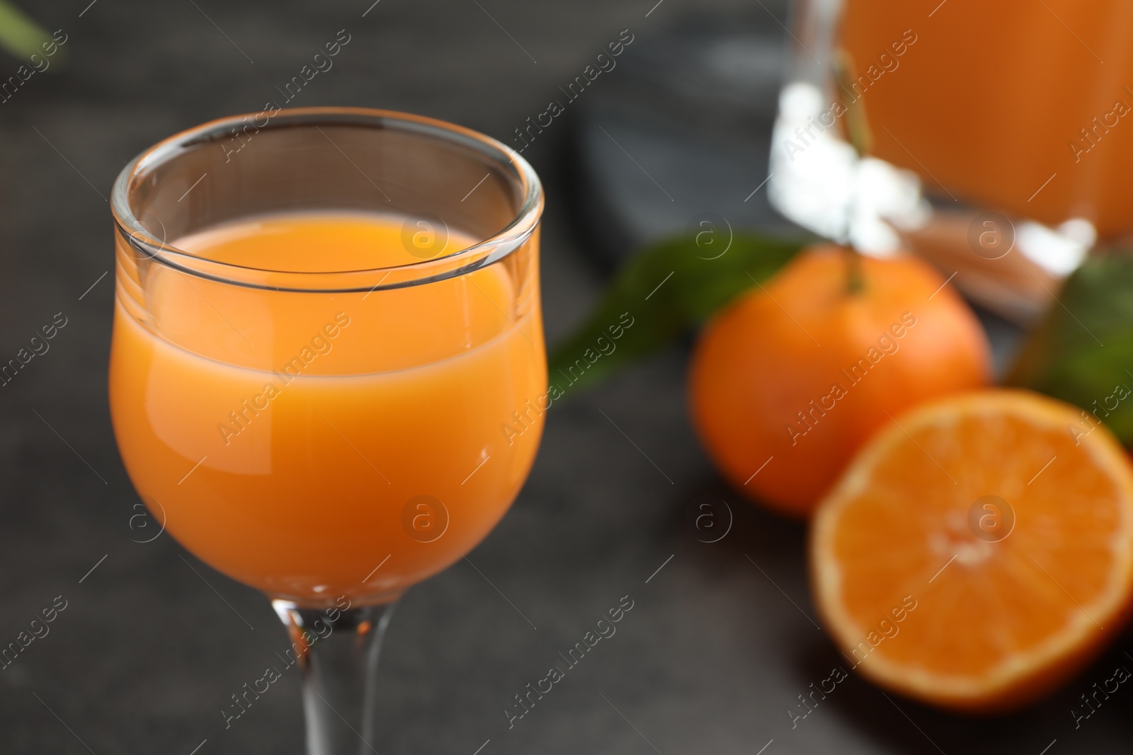 Photo of Delicious tangerine liqueur in glass on grey table, closeup