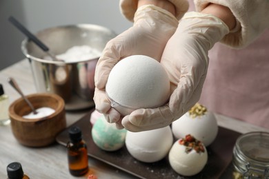 Photo of Woman in gloves with self made bath bomb at table, closeup