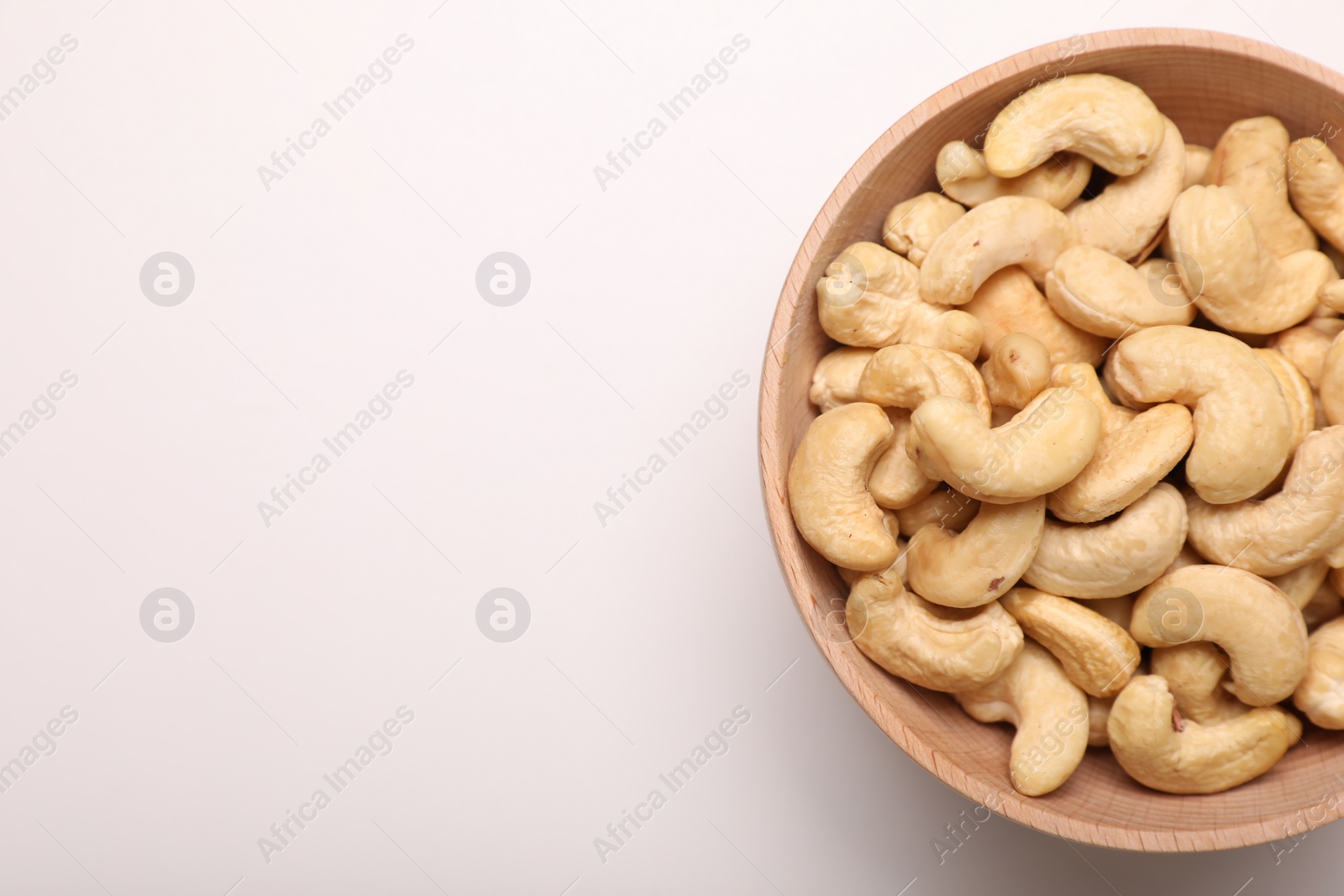 Photo of Bowl with tasty cashew nuts on white background, top view. Space for text