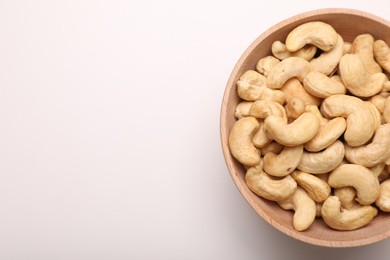 Bowl with tasty cashew nuts on white background, top view. Space for text