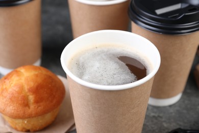 Photo of Coffee to go. Paper cups with tasty drink and muffin on table, closeup