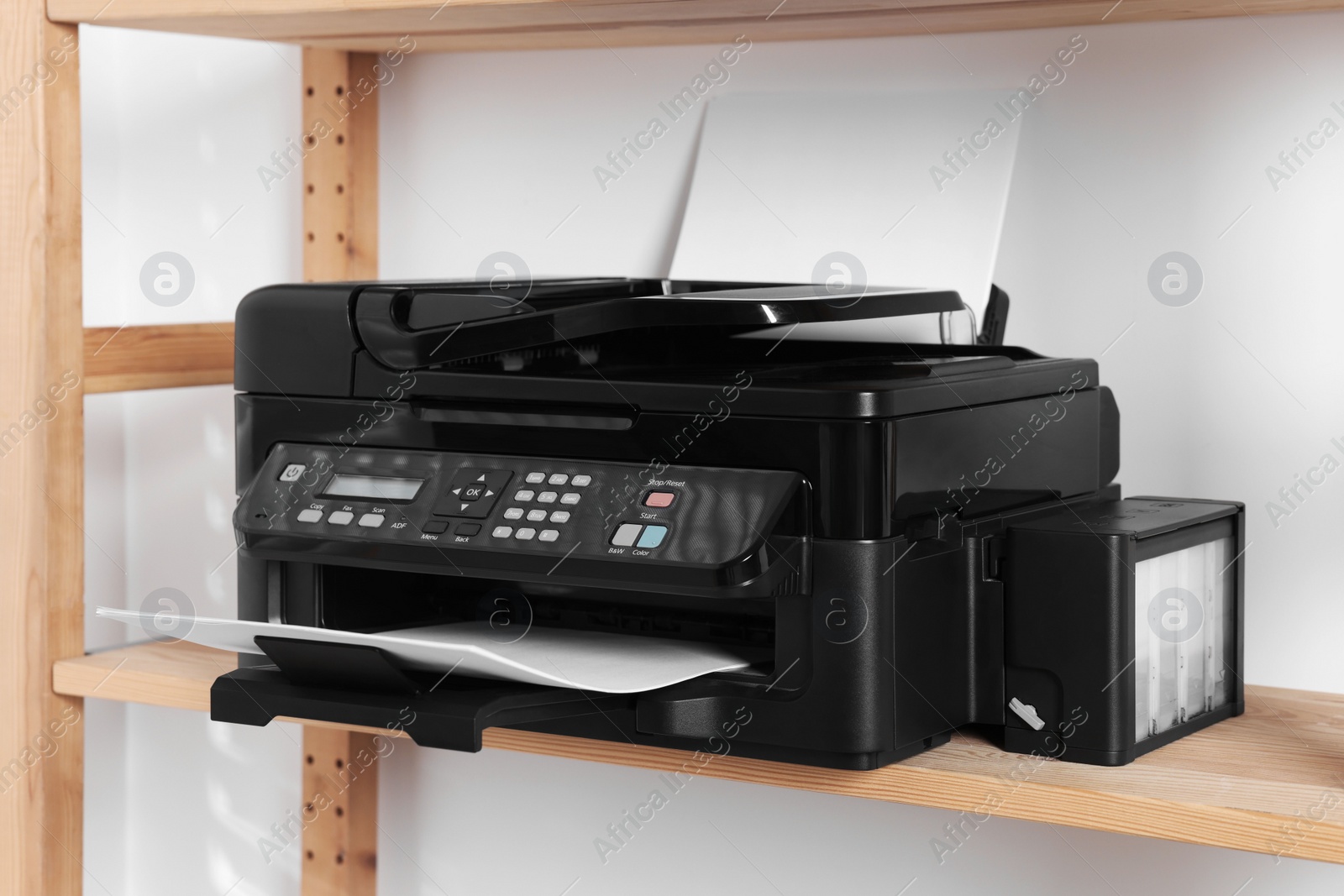 Photo of Modern printer with paper on wooden shelf in home office