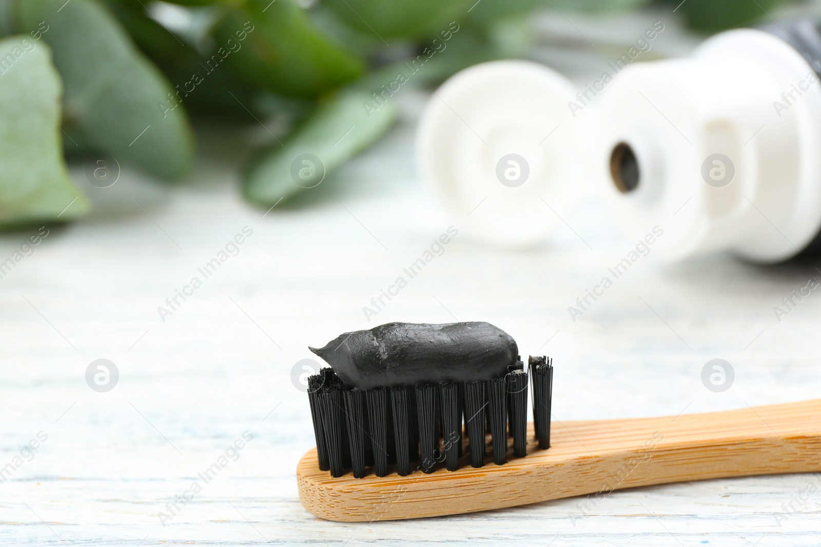 Photo of Bamboo toothbrush with charcoal paste on white wooden table, closeup. Space for text