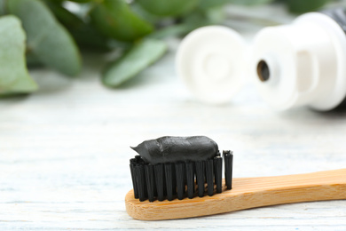Photo of Bamboo toothbrush with charcoal paste on white wooden table, closeup. Space for text