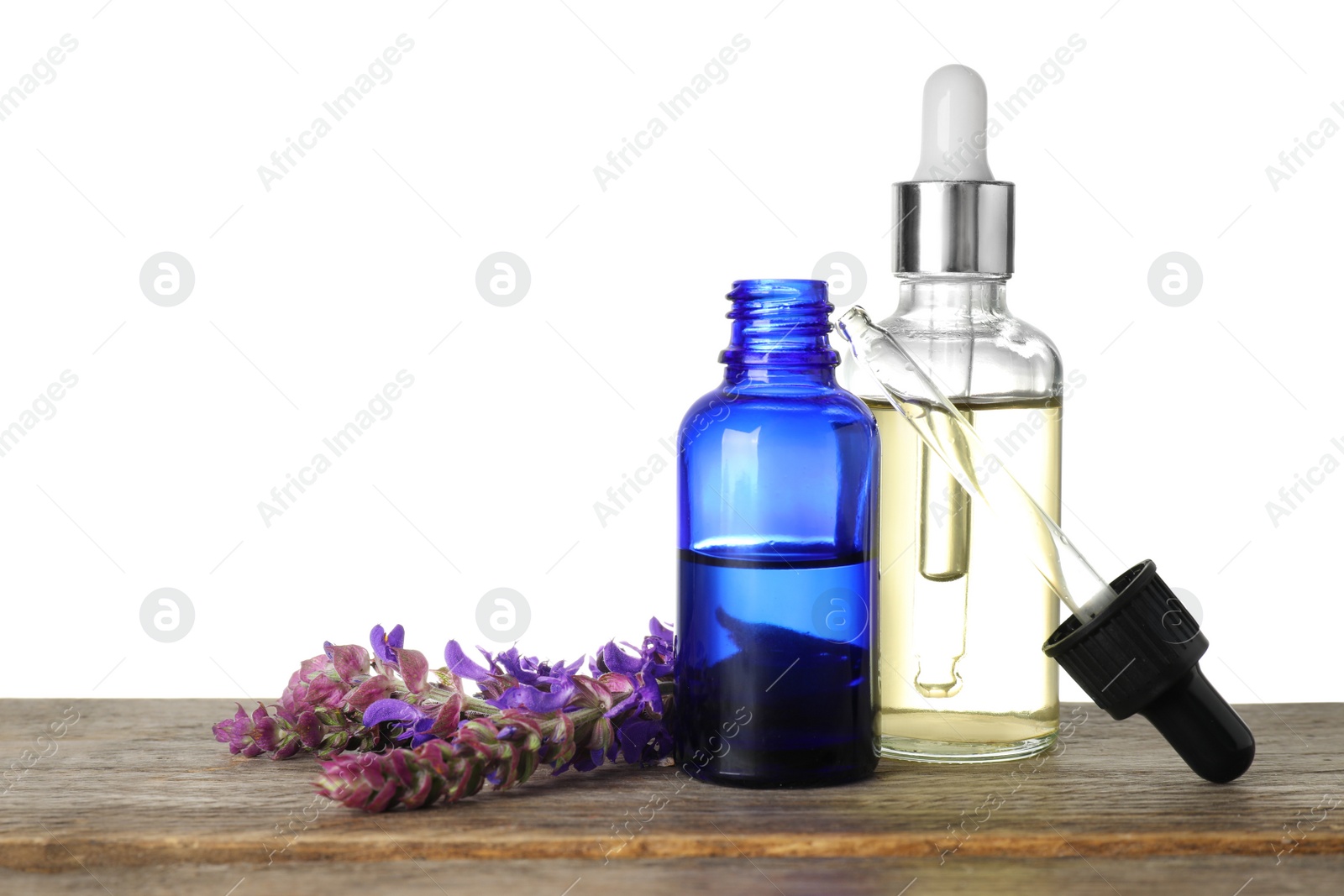 Photo of Bottles of sage essential oil and flowers on wooden table, white background