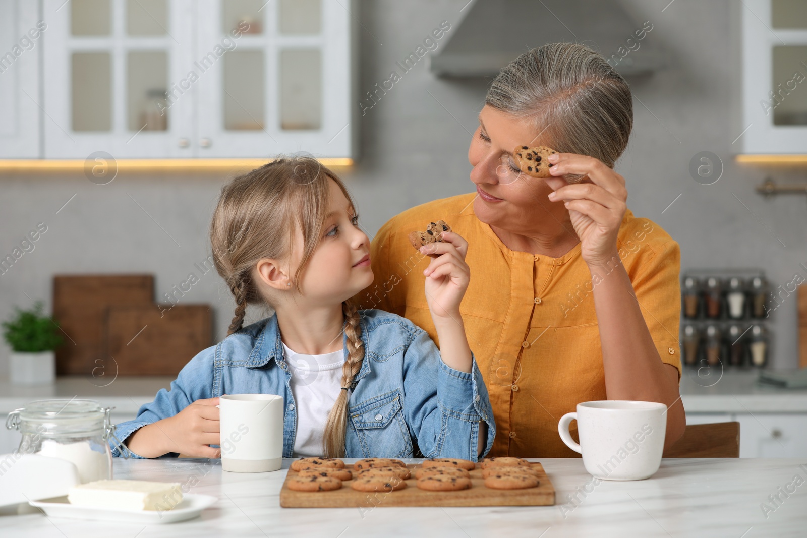 Photo of Happy grandmother with her granddaughter eating cookies in kitchen