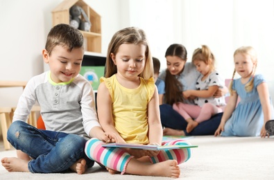Photo of Cute little children reading book together indoors, space for text. Learning and playing