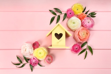 Photo of Stylish bird house and fresh eustomas on pink wooden background, flat lay