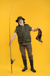 Confused fisherman with rod and old boot on yellow background