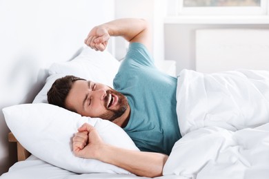 Photo of Happy man stretching on comfortable pillow in bed at home
