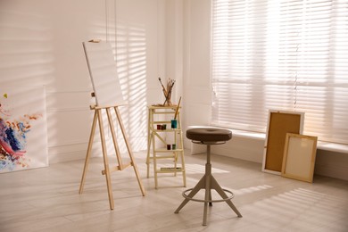 Photo of Wooden easel with empty canvas and stool in art studio