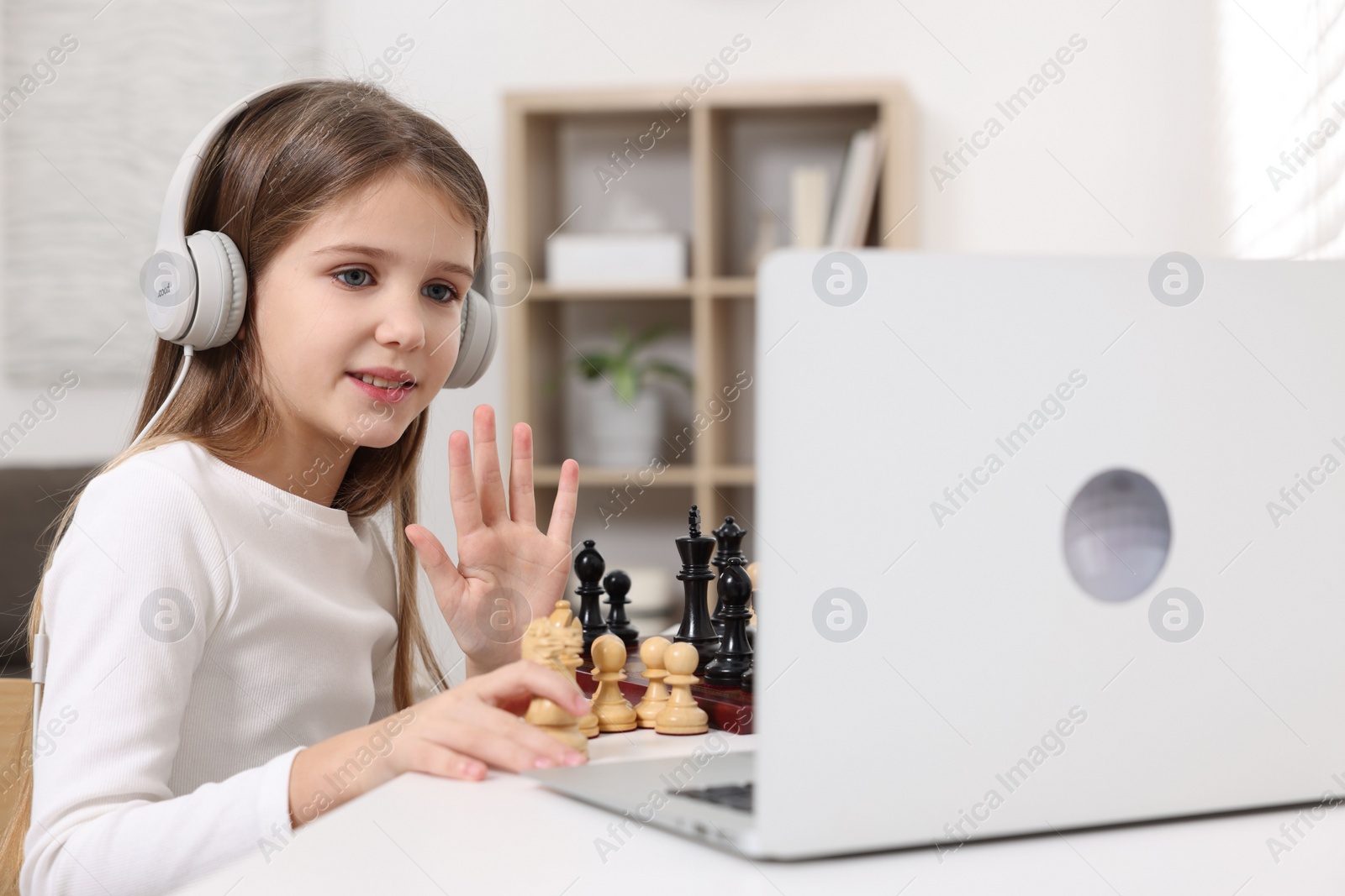 Photo of Cute girl learning to play chess with online tutor at home