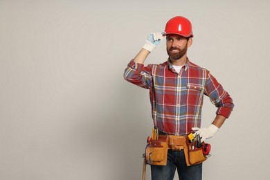 Photo of Professional builder in hard hat with tool belt on light background, space for text