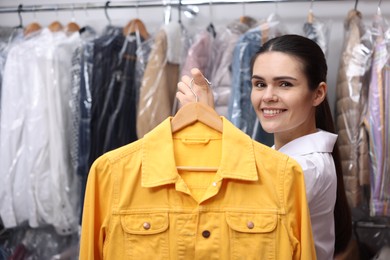 Dry-cleaning service. Happy worker holding hanger with jacket indoors