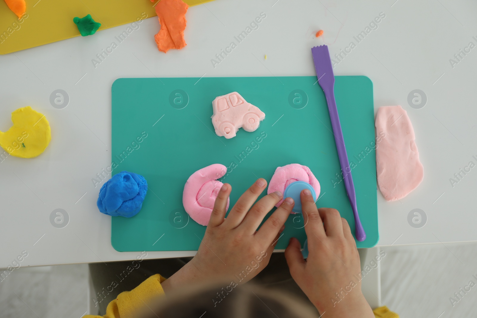 Photo of Little girl sculpting with play dough at white table, top view