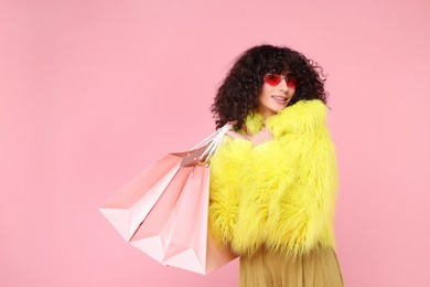 Happy young woman with shopping bags on pink background