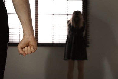 Photo of Closeup of man's fist and blurred woman indoors, space for text. Stop sexual assault