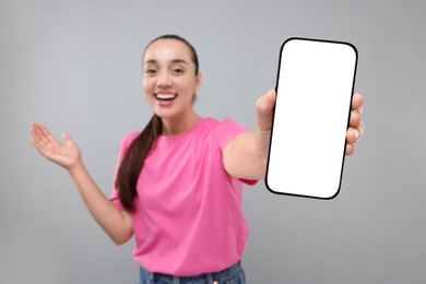 Photo of Young woman showing smartphone in hand on light grey background, selective focus. Mockup for design