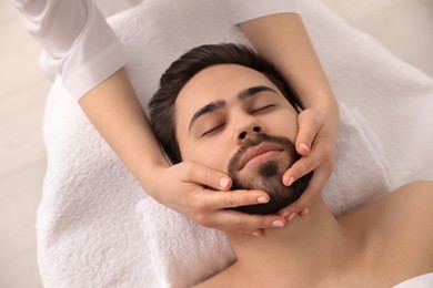 Photo of Young man receiving facial massage in beauty salon, above view