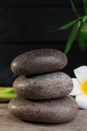 Photo of Stacked spa stones, bamboo and flower on wooden table, closeup