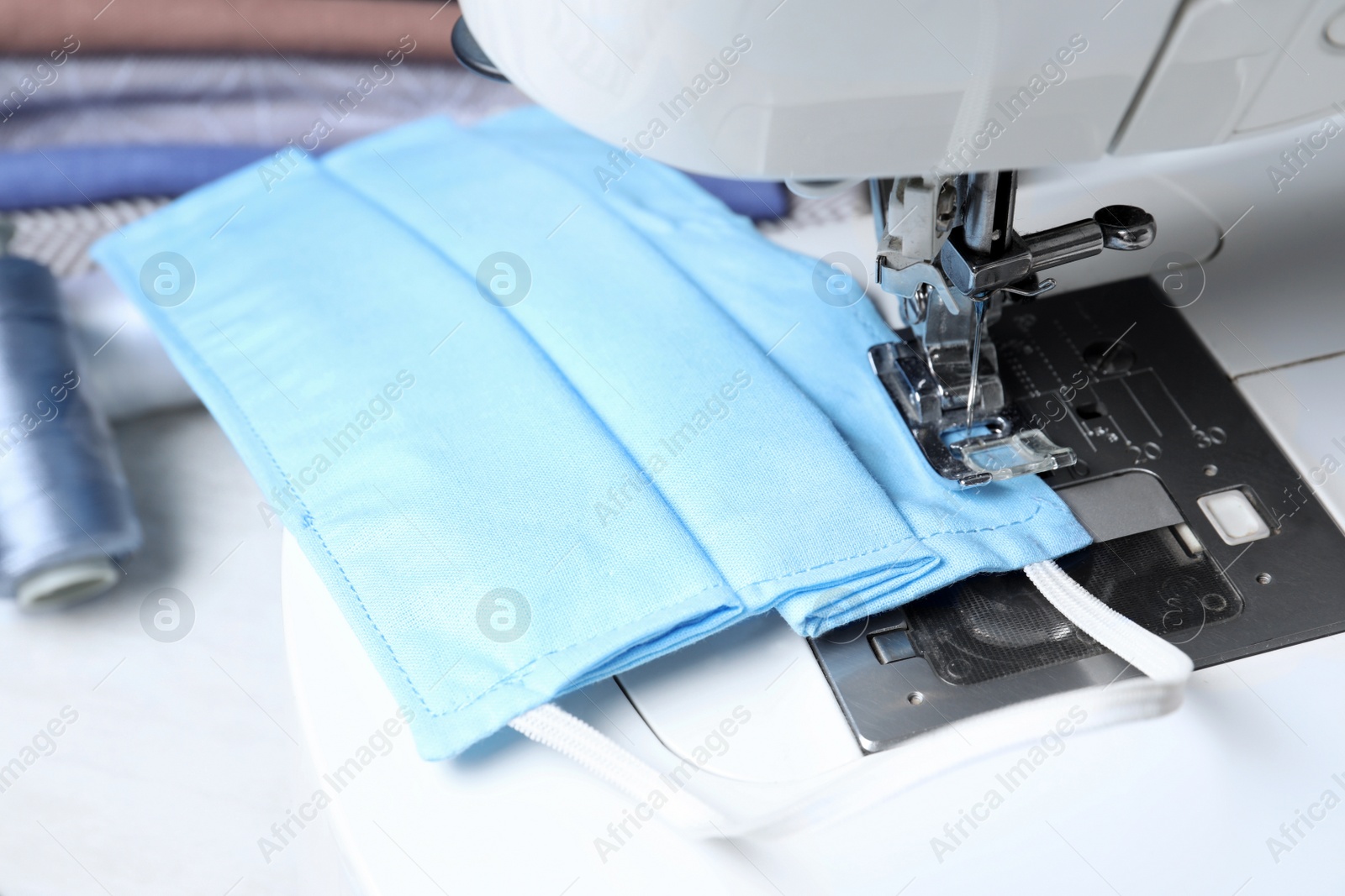 Photo of Sewing machine with homemade protective mask on table, closeup