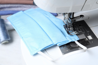 Photo of Sewing machine with homemade protective mask on table, closeup