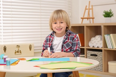 Photo of Cute little boy with glue stick at desk in room. Home workplace