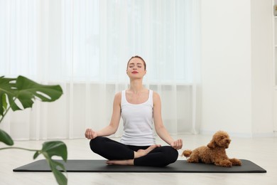 Photo of Young woman practicing yoga on mat with her cute dog indoors