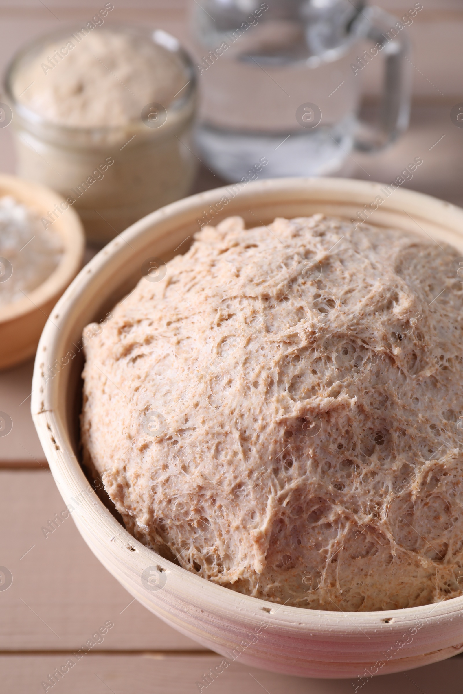 Photo of Fresh sourdough in proofing basket on wooden table, closeup